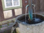 Der Brunnen steht vor dem Handwerkerhaus in der Kuhstraße in Blomberg. An dem Handwerkerhaus ist auf einer Hinweistafel zu lesen : "Handwerkerhaus mit Mitteldiele, erbaut nach 1740 von dem Schuhmacher Joh. Christoph Sauerländer (Heirat mit A.Elisabeth Recker 1740). Diele mit ehem. Herdraum und Ställen im Hinterhaus erhalten, zwei Stuben zur Straße."